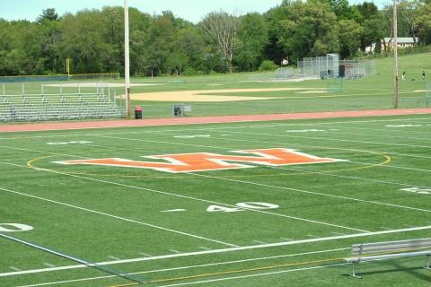 Above is a picture of the Wayland High School turf. Wayland High School graduate Ben Porter writes in support of coach Scott Parseghian. It isn’t an exaggeration to say Coach P bleeds orange and black, Porter said. (Credit: Matthew Gutschenritter / WSPN)