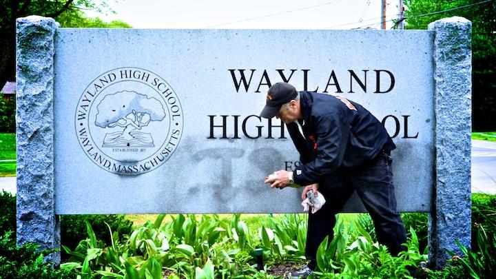 A custodian attempts to remove graffiti from the Wayland High School sign. (Photo Illustration: Jake Adelman/WSPN)