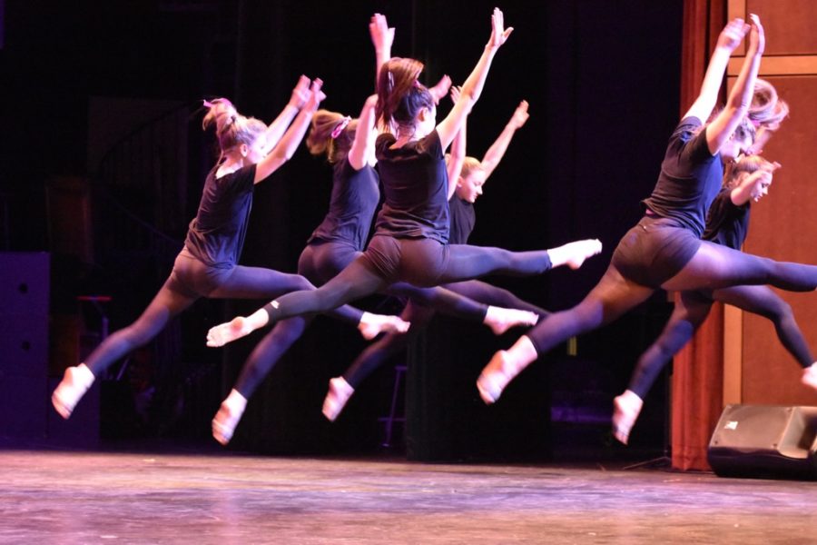 The dancers leap through the air during a ballet routine. 