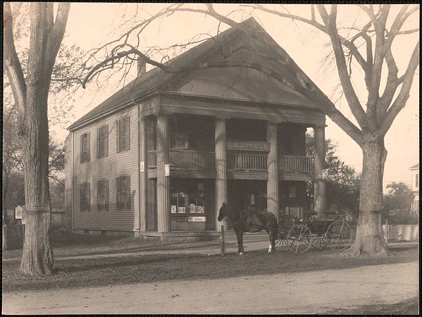 First town hall and library, built 1841. It eventually became Lovell’s Grocery and then Collins’ Market. This photograph, circa 1884-1900, shows the building as it was when it functioned as Lovells Grocery. The building was originally erected in order to serve as Waylands first town hall, and was referred to as the Town House. The first floor was a large classroom used by Wayland Academy (a private school) from 1841-1842, after which it was used as a public school. The Wayland Free Public Library used it from 1850-1878 and the town meeting hall was on the second floor. The building ceased to act as a town building in 1878 when a new town hall was built on the Grout-Heard House site. In 1879, Lorenzo M. Lovell bought the building and converted it to a dry goods and grocery store. In about 1922, Lawrence Collins leased the building from Lorenzo Lovells son, William S. Lovell, and it was used as a meat market and food store into the late 1980s. The building served as a grocery store and market for over 100 years.