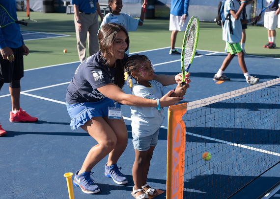 A volunteer who works with the organization ACEing Autism helps a little girl hold a tennis racket. ACEing Autism is an organization that was started to help kids with autism learn how to play tennis and there are many volunteers that help out.