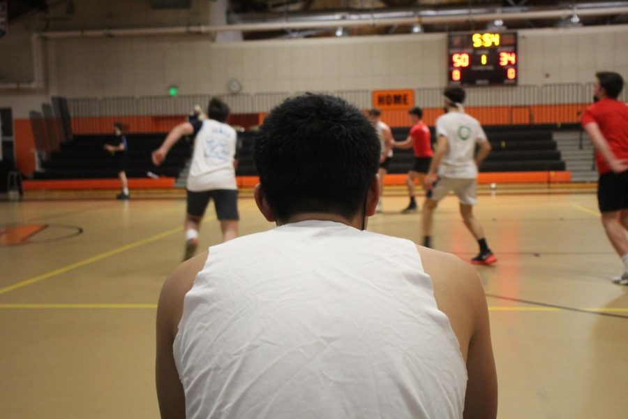 Senior Taylor Hsu watches his team from the sidelines. The scoreboard reads 50-34 towards the end of the game as the white team maintains their lead.