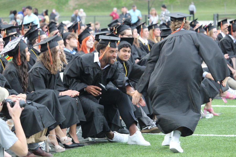 After students cross the stage, many of their classmates in the front row meet them with open high-fives.