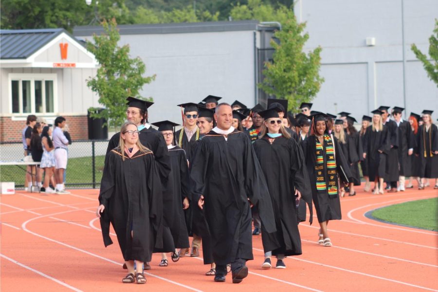 Class of 2022 advisors Jennifer Reed and Scott Parseghian lead the line of seniors down the track as they enter the turf field.