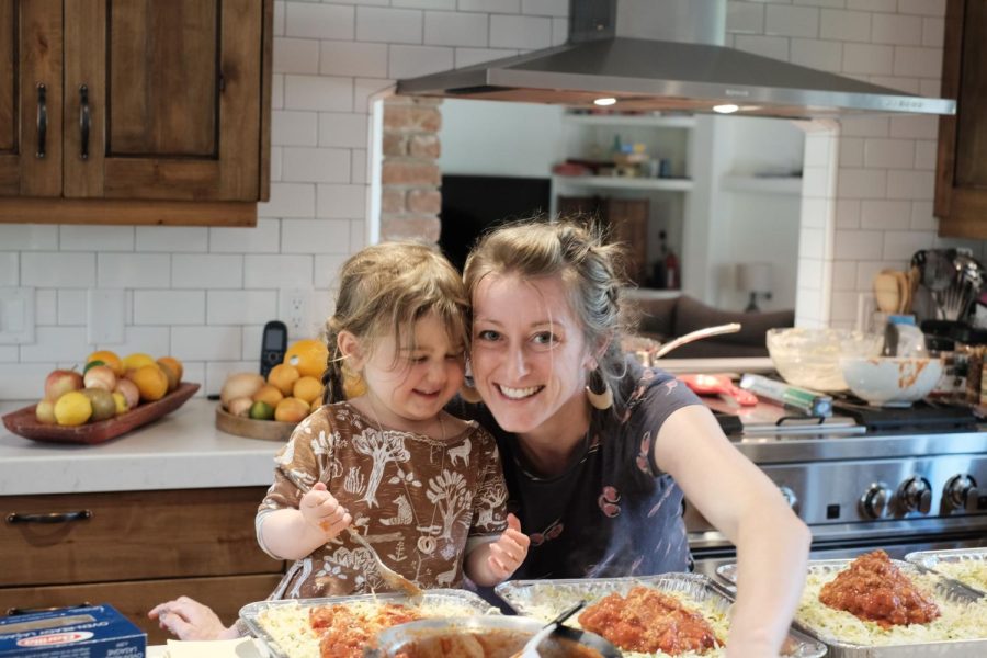 Lasagna Love founder Rhiannon Menn leans in near her young daughter as they both spoon sauce into lasagna pans. The organization was founded through Menns desire to help families who were in need during the pandemic and has now expanded to anyone in a hardship. 