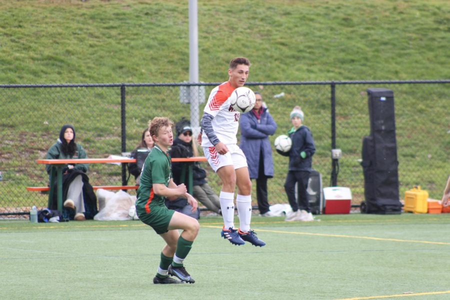 Junior Xande Santos jumps higher than a Hopkinton player to head the ball and pass it to another Wayland player.