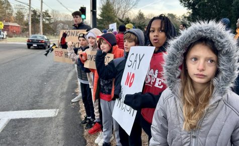 Elementary schoolers stand on the curb with signs and chant to the drivers. A parent organized a chant among the children.