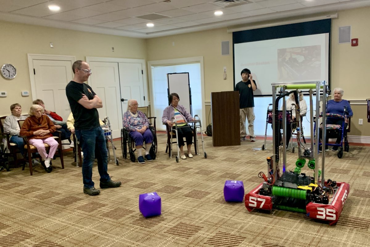 Senior residents of Carriage House observe as the Wayland High School robotics team presents its robot to the group. This past month, WHS nationally recognized robotics team brought their robot to the assisted living facility to display for the seniors. “We went to Carriage House to show off our robots to the senior citizens because they are always looking for more activities to brighten up their days,” WHS senior captain Charmaine Guo said. “[The seniors] love talking to me about my robotics and so we did [a demonstration] last year where we brought the robot in and we did it again this year.”