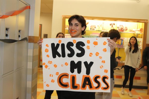 Senior Student Council Vice President Giovanni Sebastianelli covers his lips in orange paint to cover a poster titled Kiss My Class with kisses.