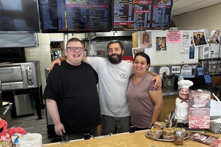 Liberty’s Pizza owners Sam (middle) and Shery (right) Maksimous are pictured behind their shop’s front desk with a customer. On Oct. 3, the auto body shop in the Cochituate Plaza caught on fire, causing significant smoke damage to Liberty’s. “We lost our lives,” owner Shery Maksimous said. “The business is like our home [since] we’re not from here. My husband and I have fought to get a good life for us and our four kids. When [the fire] started, it [hurt us because] our whole family’s [sacrifices] were in the store. My kids grew up there.”
