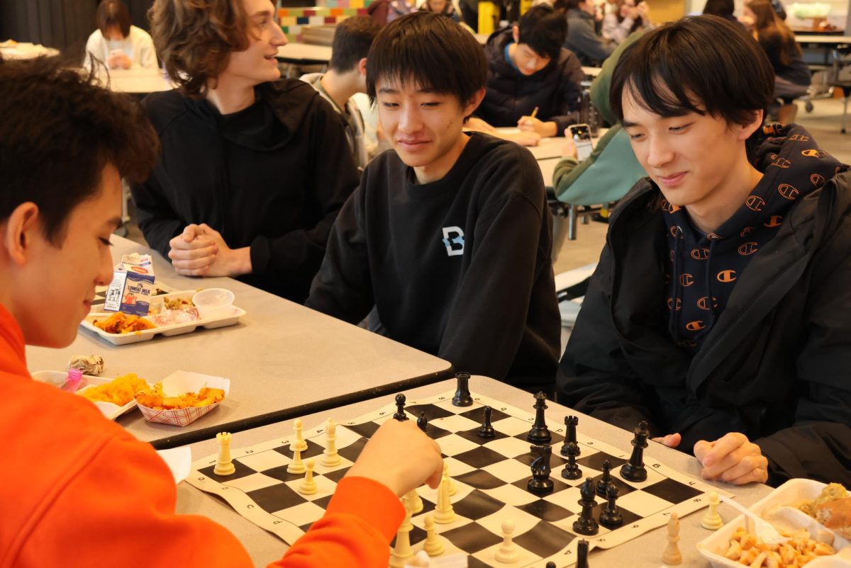 Junior Henry Han (far left) watches a chess match between junior Josh Proctor (left) and senior Andrew Fang (right). 