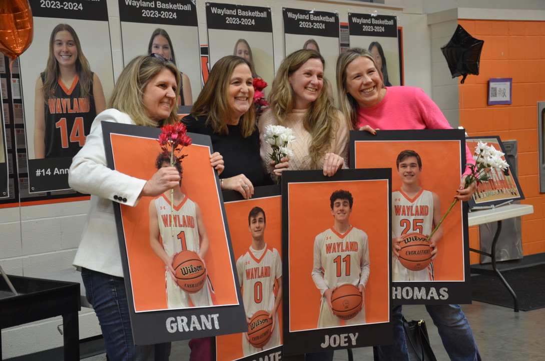A group of moms hold up their sons senior signs to pose for a photo.