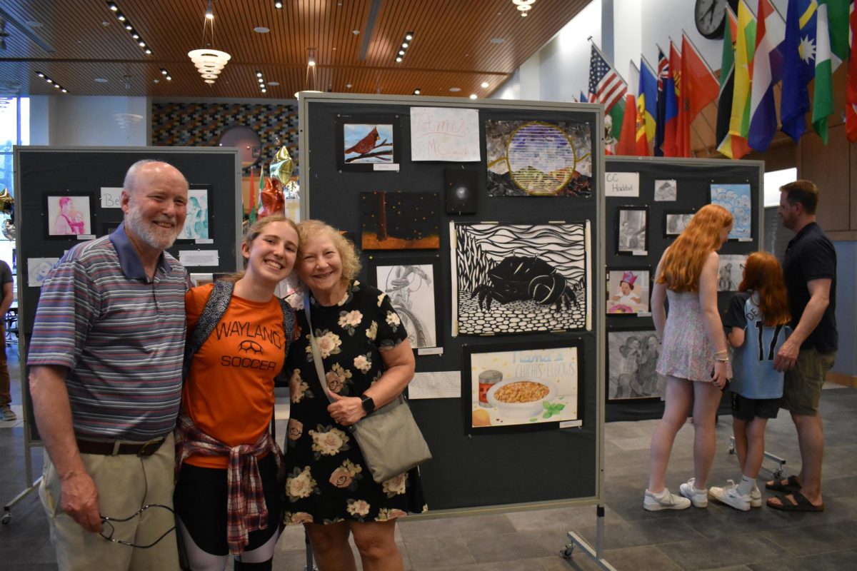 Senior Amy McCormack smiles with her family in front her artwork. McCormacks theme displayed different scenarios that reminded her of home, time spent in nature and portraits of her family members.