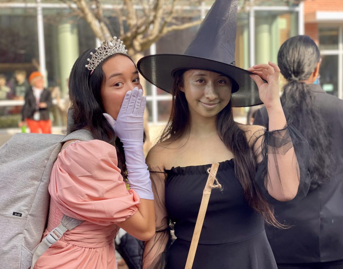 Posing for the camera to mimic the upcoming "Wicked" musical's movie cover, senior Denedra Ma (left) whispers in Fiona Wang's (right) ear to show off their costumes inspired by the film.