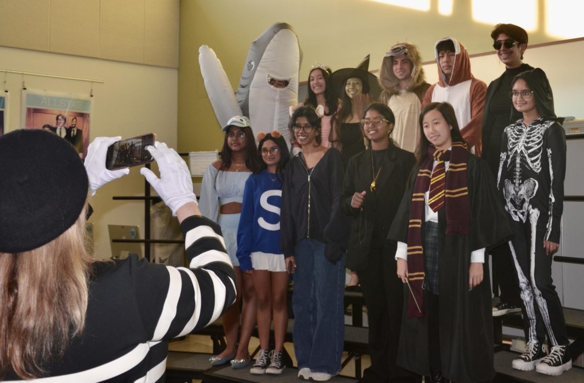 Snapping a quick picture, chorus teacher Rachel Carrol documents her Honors Concert Choir students in their costumes. Pictured in the back row from left to right Arya Samaratunga, Denedra Ma, Fiona Wang, Michael Likerman, Elliot Xu, Swara Metlapally and Sujitra Paramasivam pose on the risers. In the front row, from left to right stand seniors Aamena Syed, Annika Bangalore, Kanmani Sekhar, Pariplavi Sontha and Christina Yu.