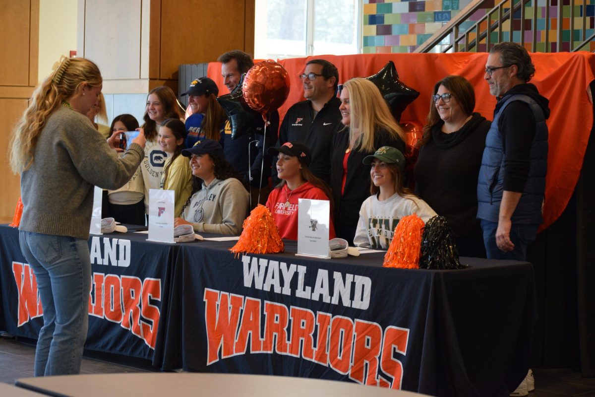 Senior Cate Ellenbogen snaps a picture of senior Jillian Mele and her family to document her commitment to the University of Vermont. Every year, Wayland Boosters organizes multiple different signings for the seniors committed to Division I, II and III sports. Join WSPN’s Sofia Ciciarelli as she covers Wayland Boosters, and how they’ve made an impact on high school athletes.