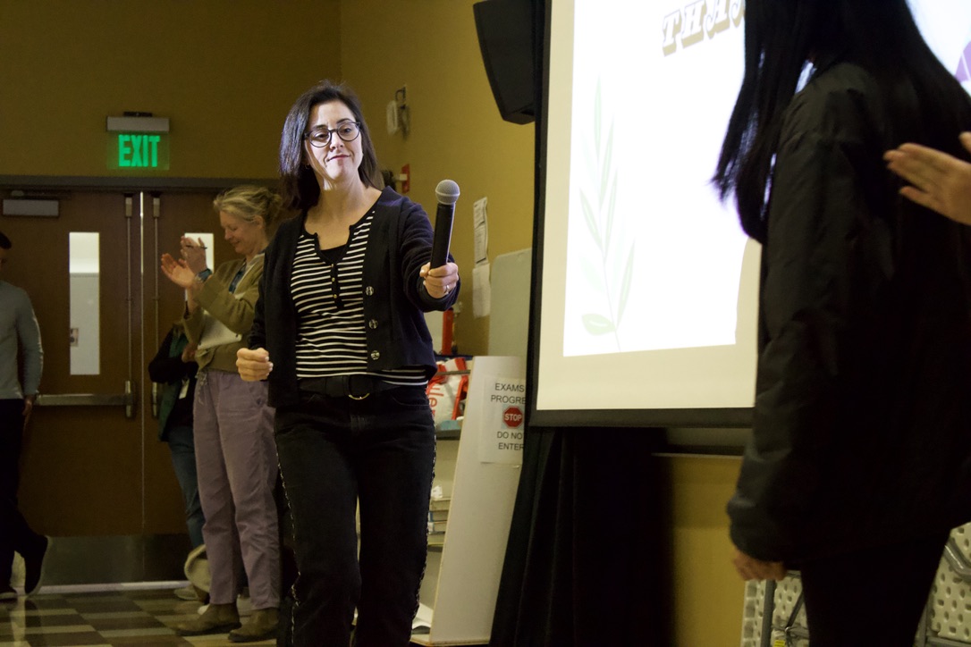 Sewing club advisor Sara Langelier hands the microphone off to one of the "slow fashion show" leaders. Langelier recognized that her entire outfit was either thrifted, revamped or sewn.