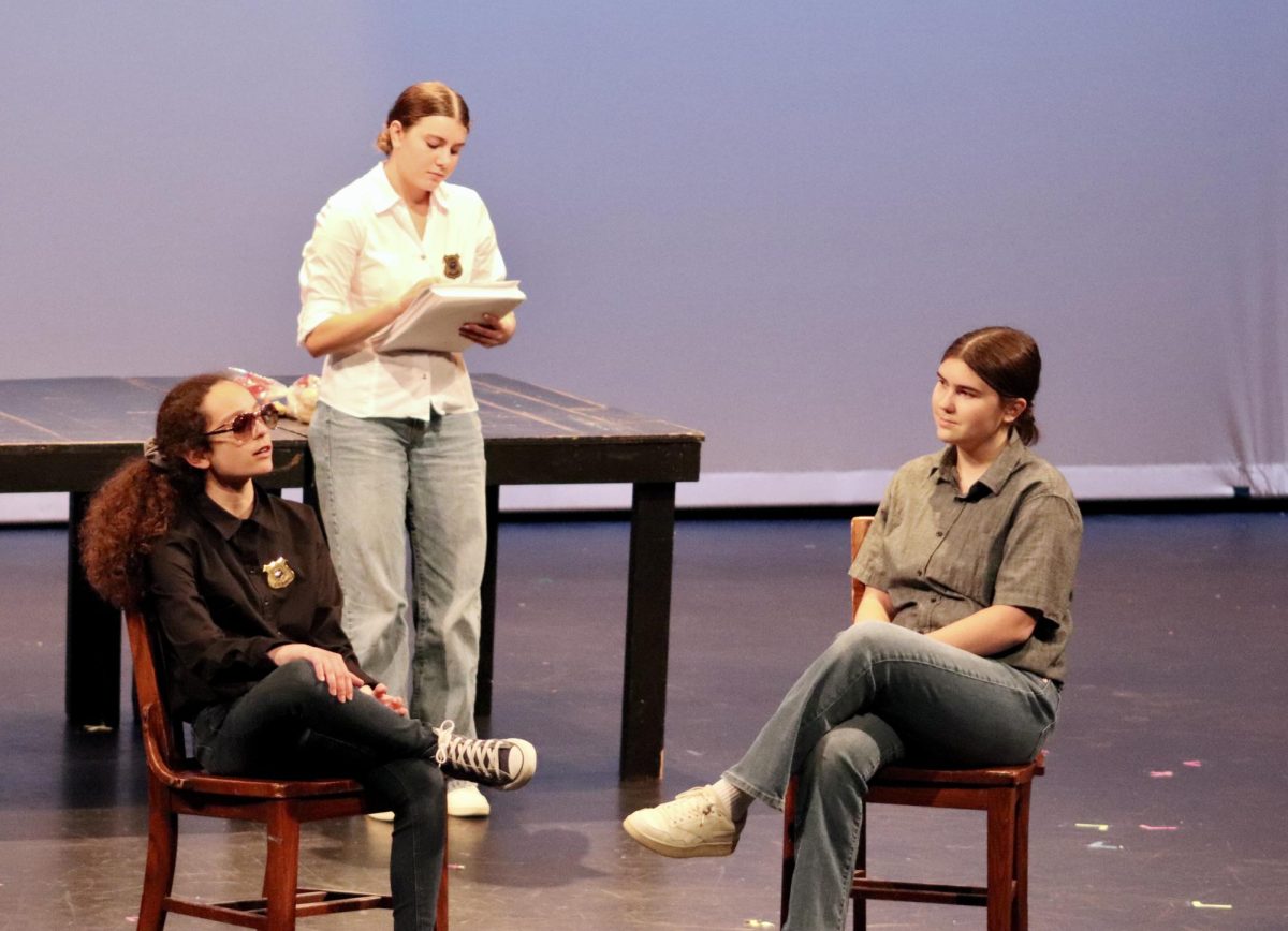 From left to right, freshman Ariana Price,  sophomore Callie Zedower and junior Ruth Flacke act out a discussion about senior writer and director George Stafford. They performed "A Gritty Play About Detectives Solving a Crime" written and directed by senior George Stafford.  The set featured NYPD mispelled as 'NIPD" and actors wearing toy police badges. "Part of my creative process was just thinking aboiut how things could go wrote due to a lazy writer," Stafford said. "Part of the joke in [my play] was that the set wasn't very good."