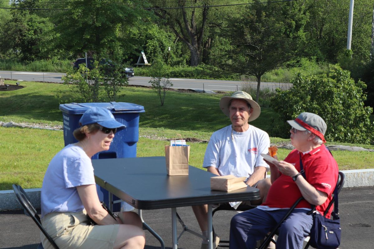 Senior citizens sit around one of the many tables set up outside while they eat pizza and chat with each other.