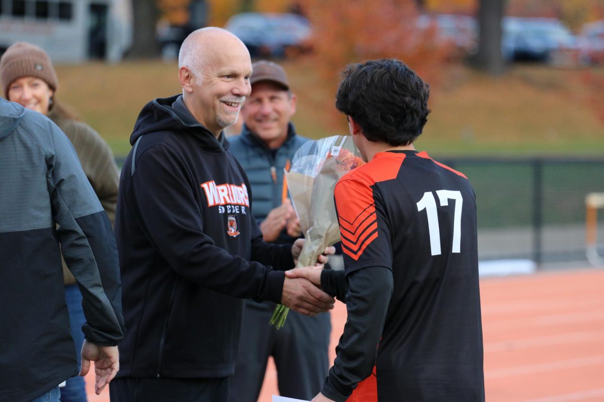Senior Max Crowe shakes hands with head coach David Gavron. After shaking hands, Coach Gavron gives a bouquet of flowers to Crowe.