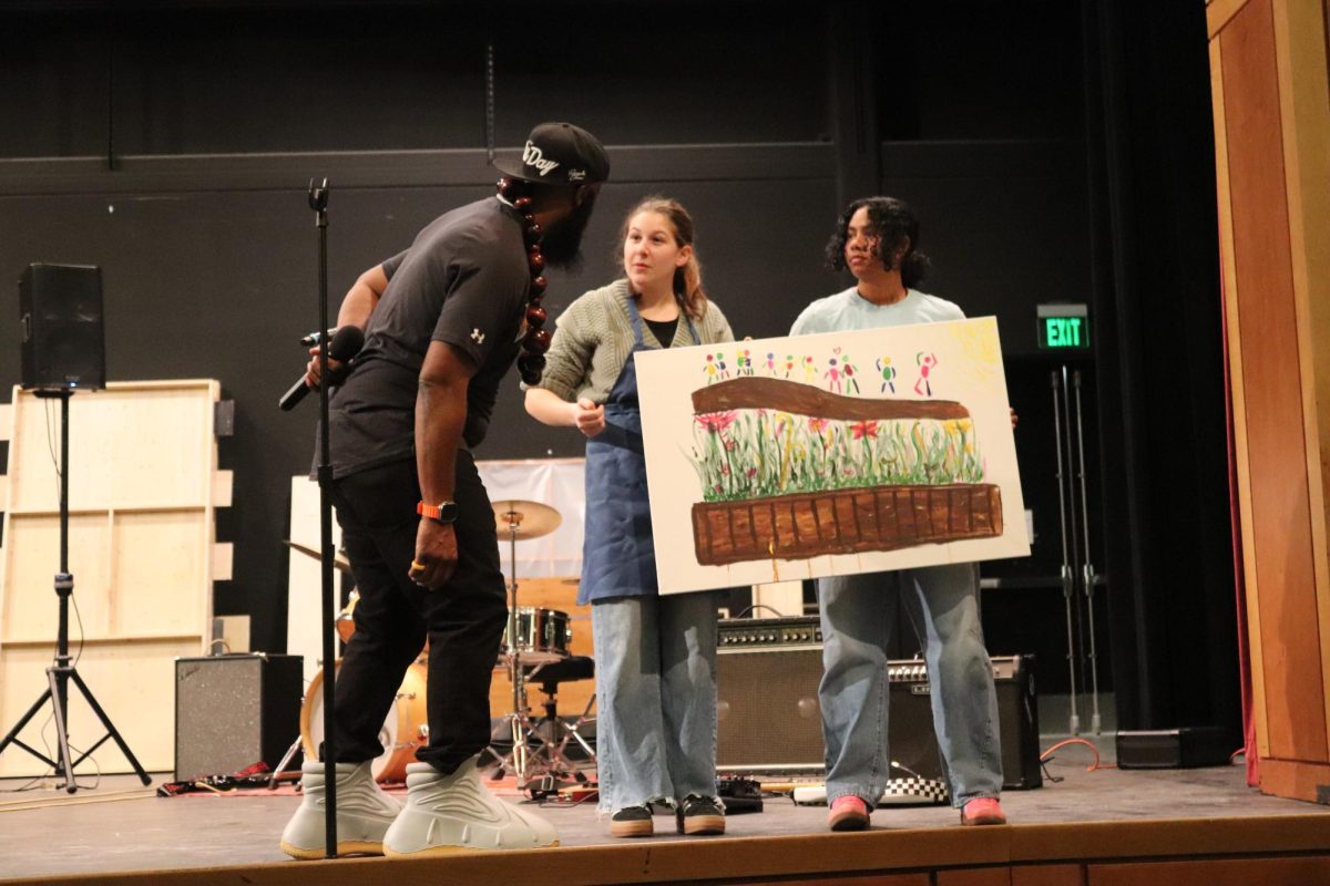 Senior Shubha Iyer and junior Frankie Zilembo display a painting created live during the assembly as jamele adams looks on.
