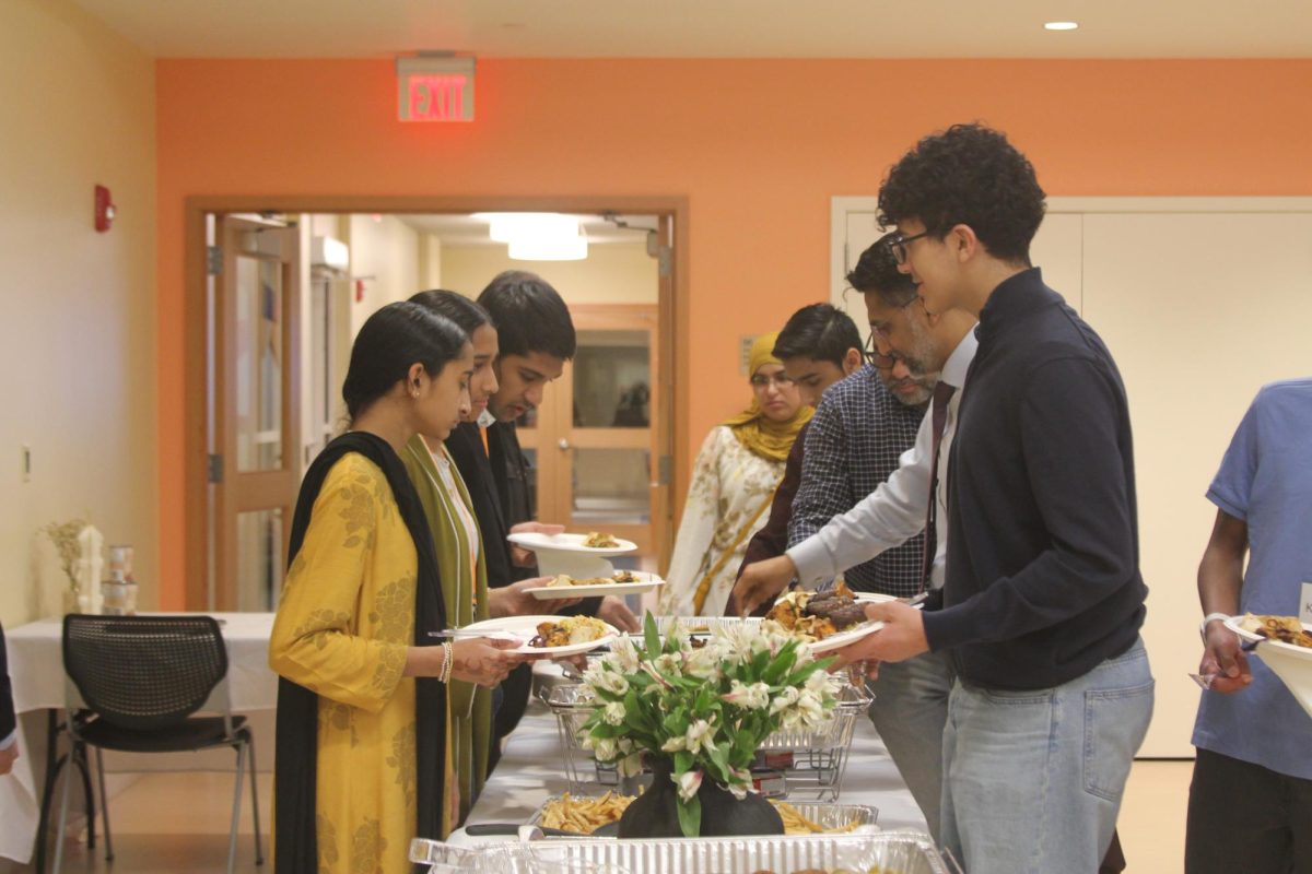 A group of students and parents serve themselves traditional Middle Eastern dishes like shawarma and lamb shish, as well as pizza and french fries.