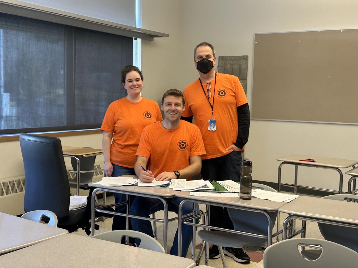 From left to right, history teachers Laine Winokur, Timothy Glavin and physics teacher Ken Rideout pose for a photo in WEA t-shirts as Glavin grades work. 