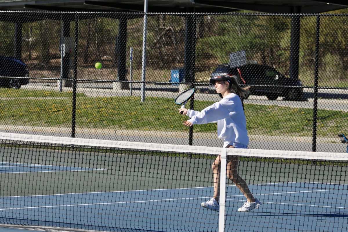 Swinging her racket to hit the ball, senior captian Ava Knourenko hits the ball over the net and earns her team a point against Cambridge Rindge and Latin School.