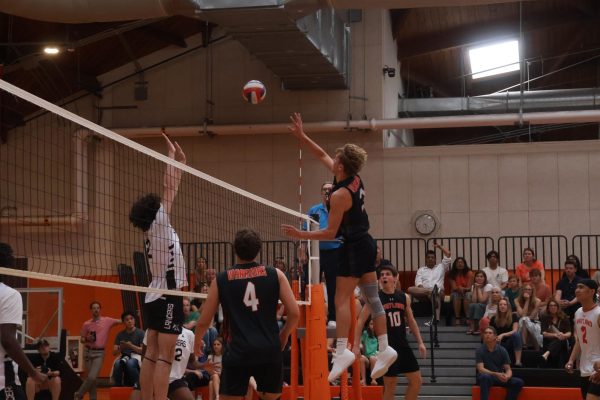 Senior Finn Bell leaps up and attempts a kill, contested by a Longmeadow defender.